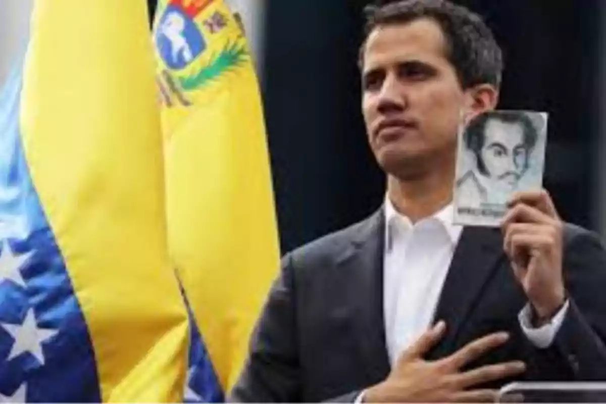 Hombre con la mano en el pecho sosteniendo un libro frente a una bandera de Venezuela.