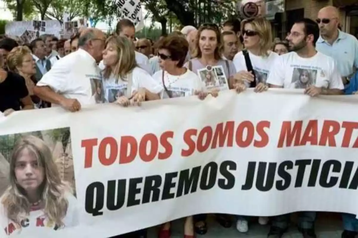 Una multitud de personas se manifiesta sosteniendo una pancarta que dice "TODOS SOMOS MARTA, QUEREMOS JUSTICIA", con la imagen de una joven en el extremo izquierdo de la pancarta.