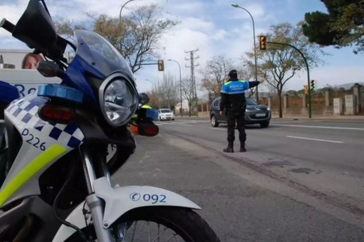 Un agente de policía de tráfico dirigiendo el tránsito en una intersección, con una motocicleta policial en primer plano.
