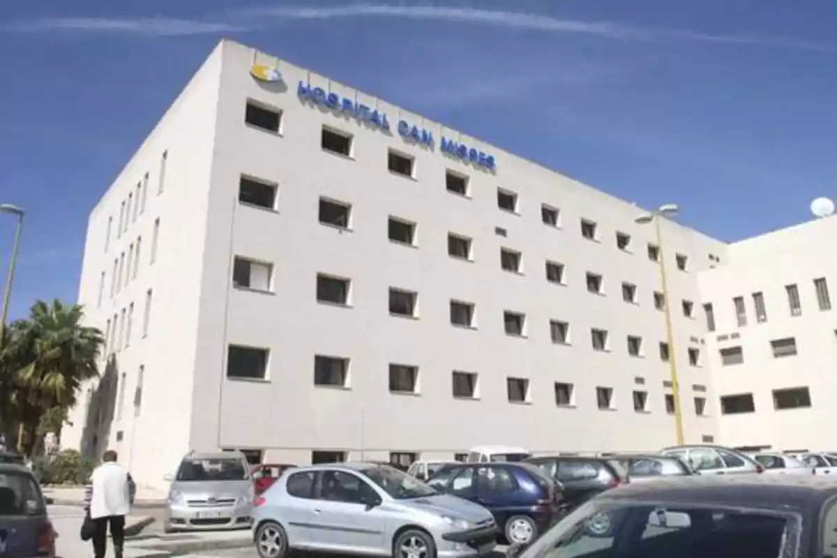 Edificio del Hospital Can Misses con varios coches estacionados en el aparcamiento frontal y una persona caminando hacia la entrada.
