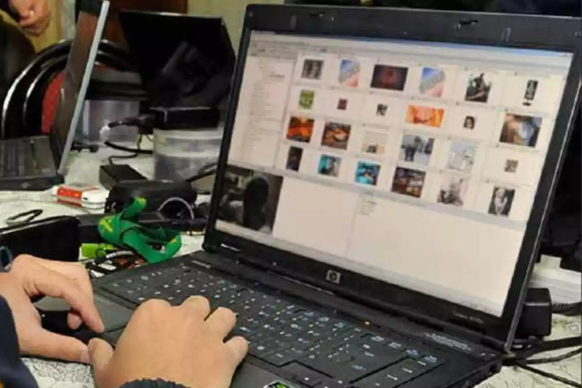 Una persona usando una computadora portátil con varias imágenes en la pantalla, rodeada de otros dispositivos electrónicos y accesorios sobre una mesa.