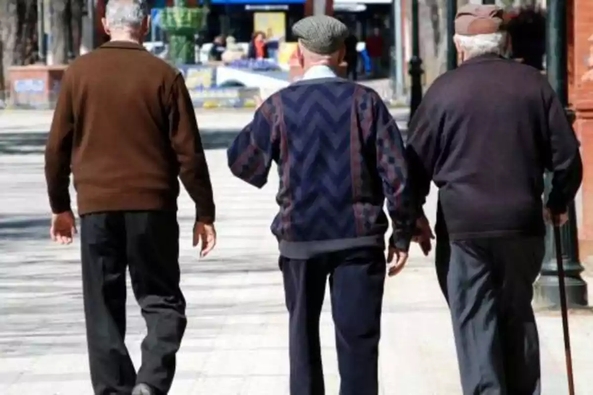 Tres hombres mayores caminando juntos por una calle.
