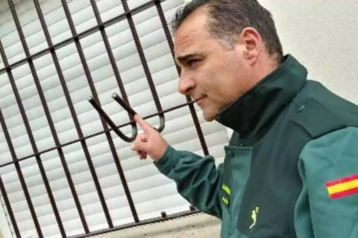 Un hombre con uniforme verde señala una reja de metal que ha sido forzada.