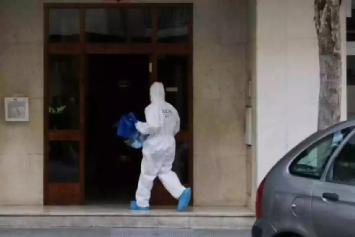 Una persona con traje de protección entra a un edificio llevando una bolsa azul.