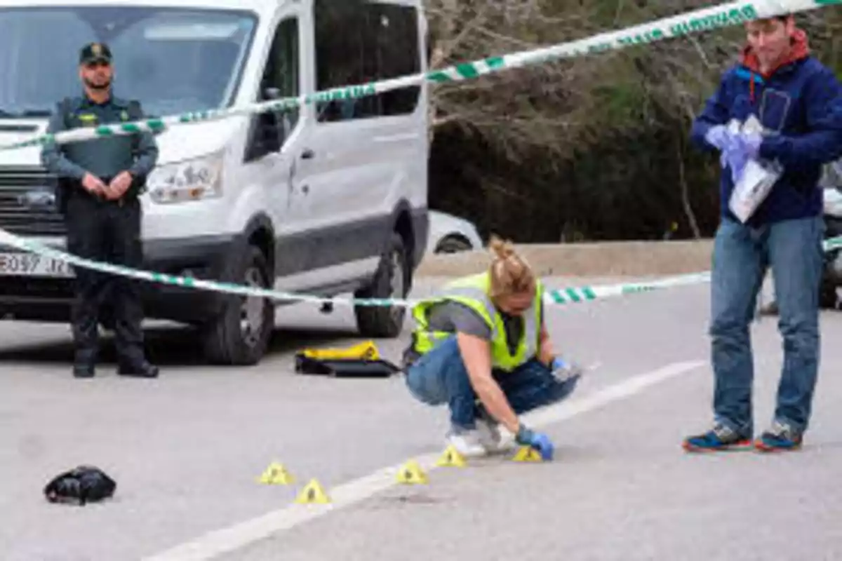 Investigadores y un oficial de policía trabajando en la escena de un crimen acordonada con cinta de seguridad, con una furgoneta blanca en el fondo.