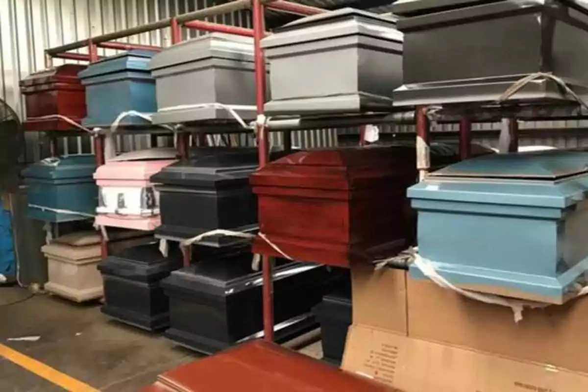 Varios ataúdes de diferentes colores apilados en estantes dentro de un almacén.
