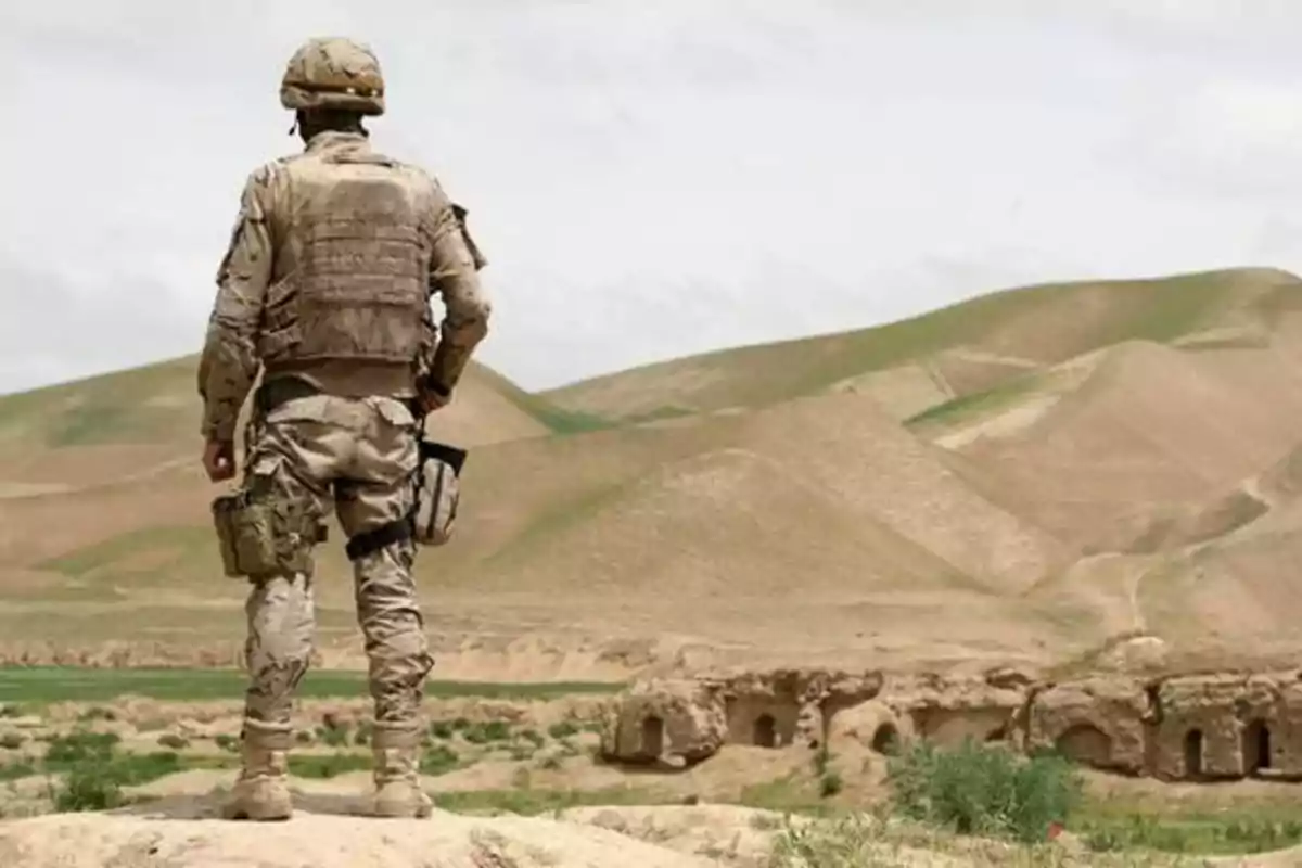 Un soldado de pie en un paisaje desértico con colinas y ruinas al fondo.