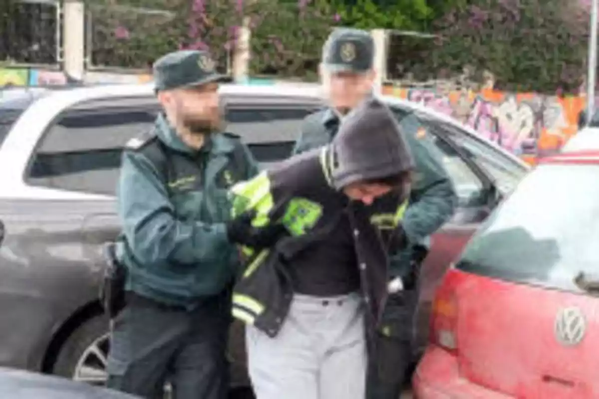 Dos agentes de policía arrestan a una persona con sudadera y chaqueta en un estacionamiento.