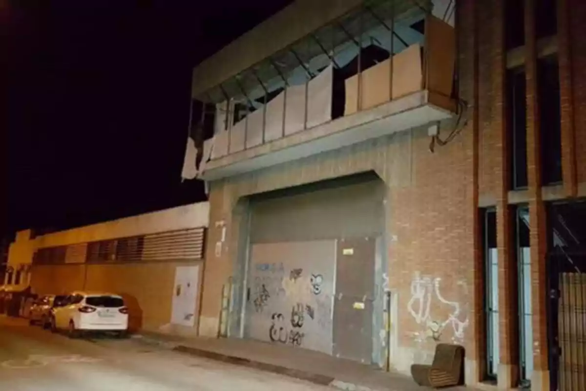 Edificio de ladrillo con grafitis en la puerta y coches estacionados en la calle por la noche.