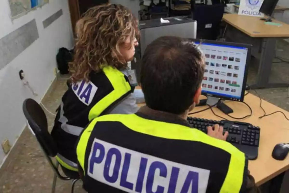 Dos policías con chalecos reflectantes trabajan en una oficina frente a una computadora.