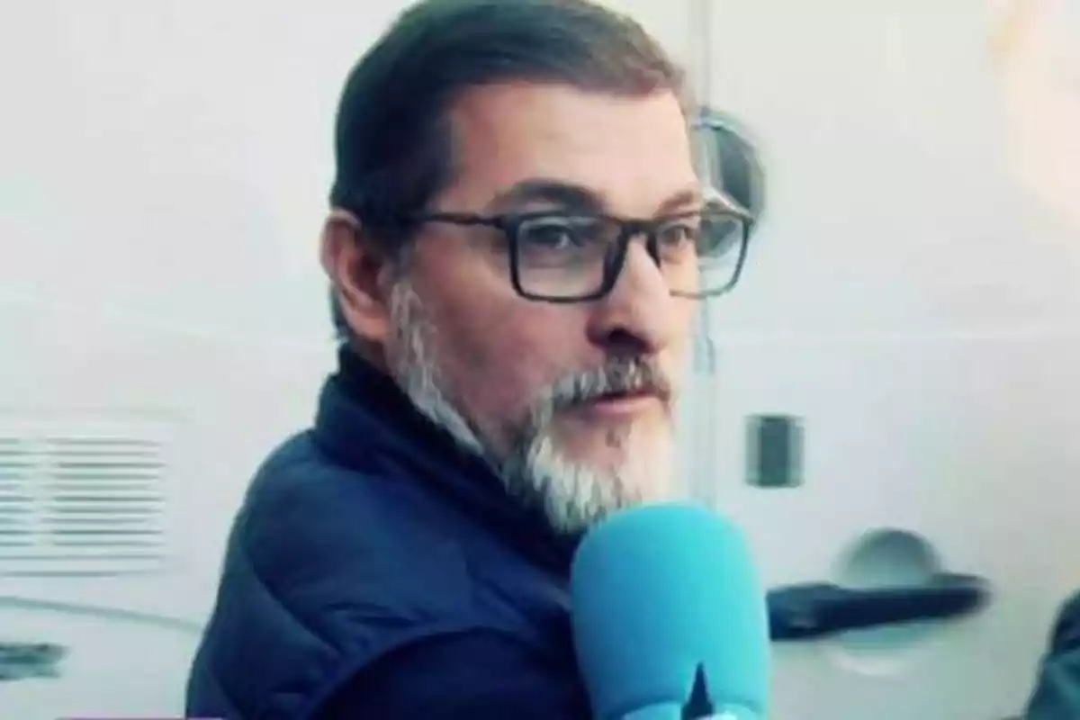 Hombre con barba y gafas sosteniendo un micrófono azul.