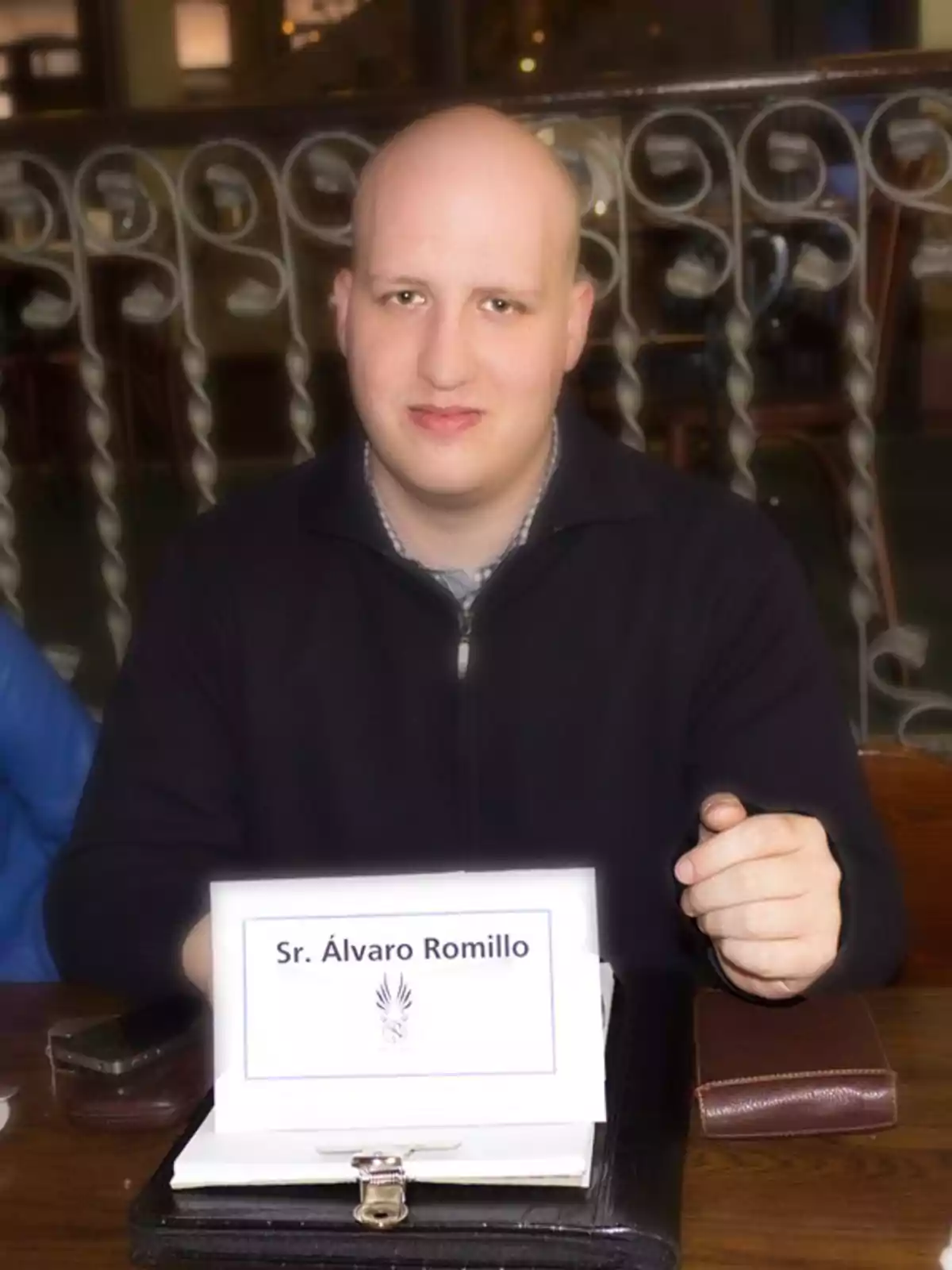 Un hombre sentado en una mesa con un cartel que dice 