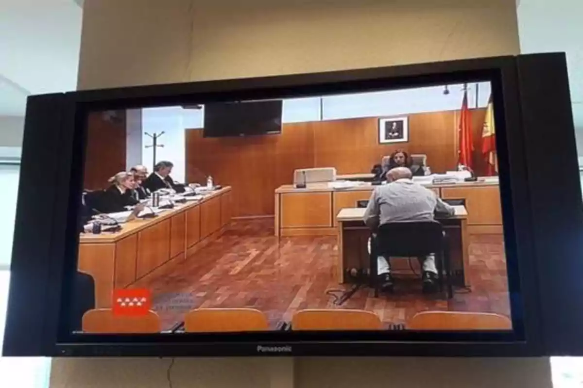 Una pantalla de televisión muestra una audiencia judicial con varias personas sentadas en una sala de tribunal.