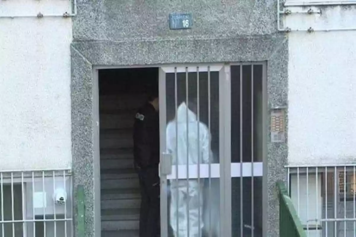 Una persona con un traje blanco y un oficial de policía están en la entrada de un edificio con el número 16.
