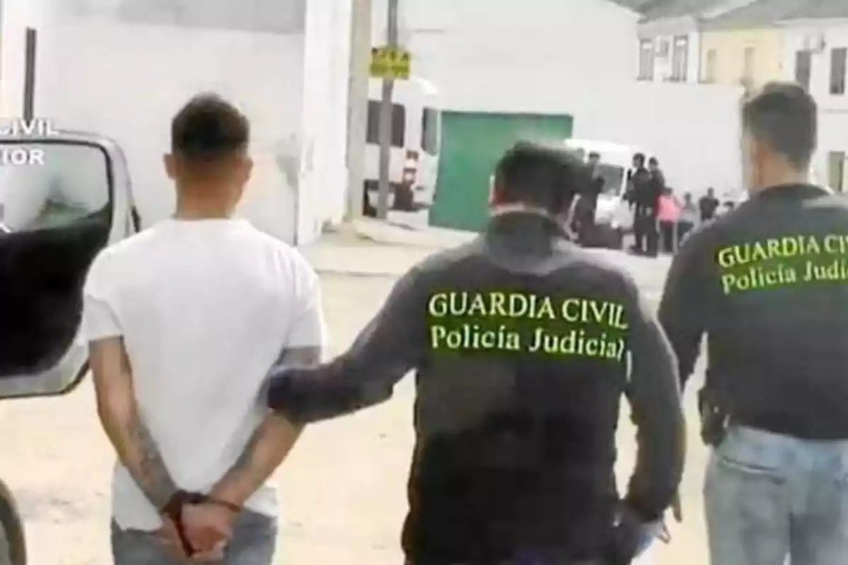 Un hombre esposado es escoltado por dos agentes de la Guardia Civil con chaquetas que dicen 