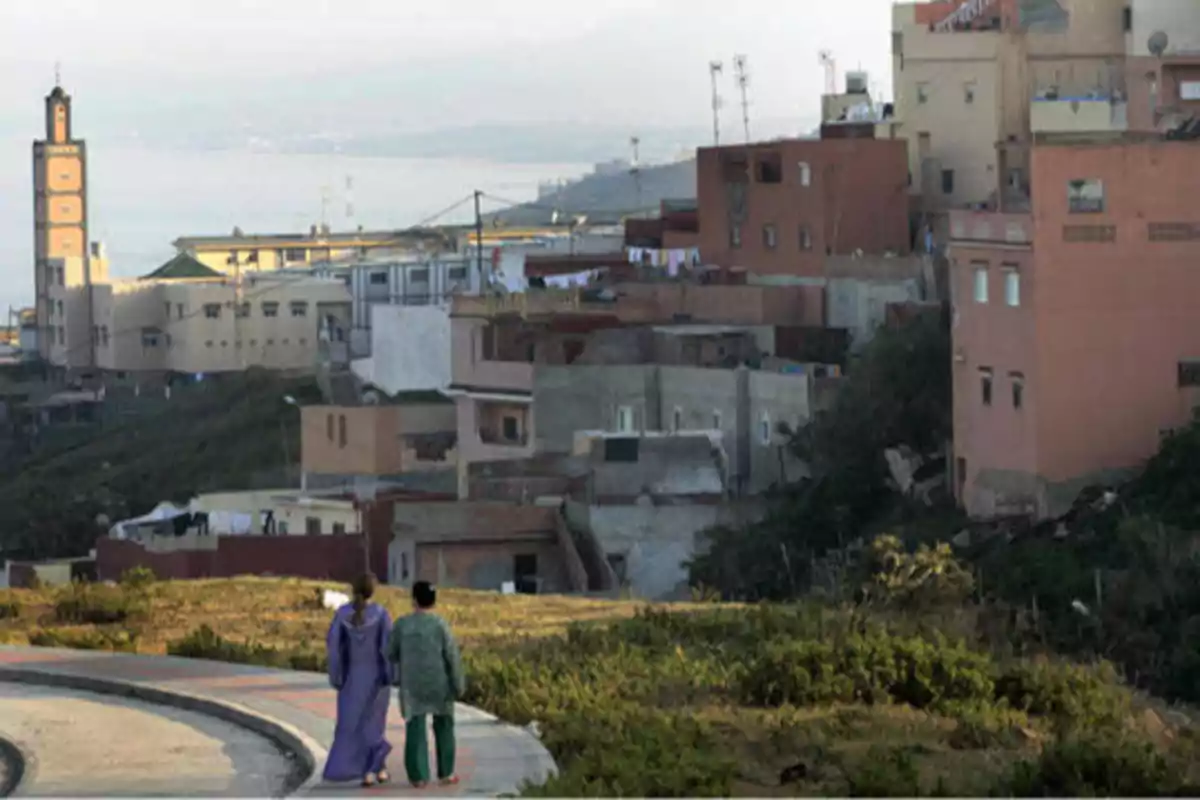 Dos personas caminando por un sendero con una ciudad y una mezquita al fondo.