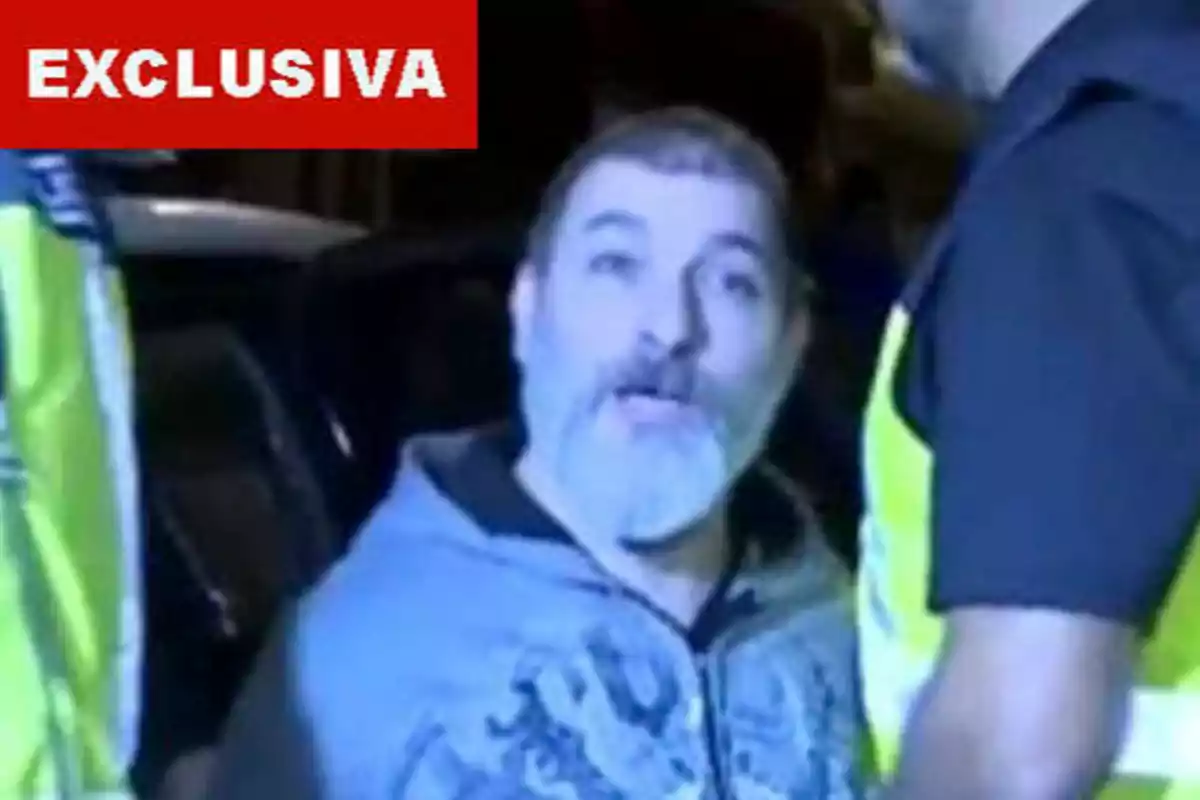 Hombre con barba gris siendo detenido por la policía, con un letrero rojo que dice "EXCLUSIVA" en la esquina superior izquierda.