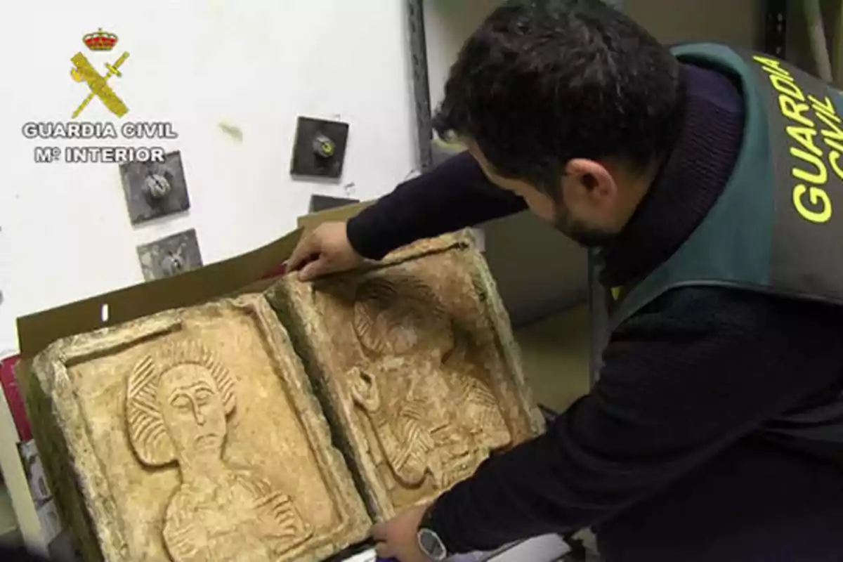 Un agente de la Guardia Civil examina dos piezas arqueológicas con figuras talladas.