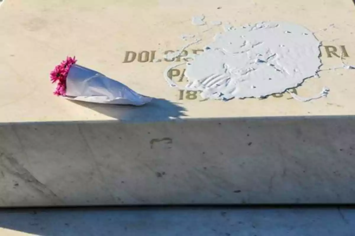 Una lápida de mármol con un ramo de flores rosadas y una mancha de pintura blanca.