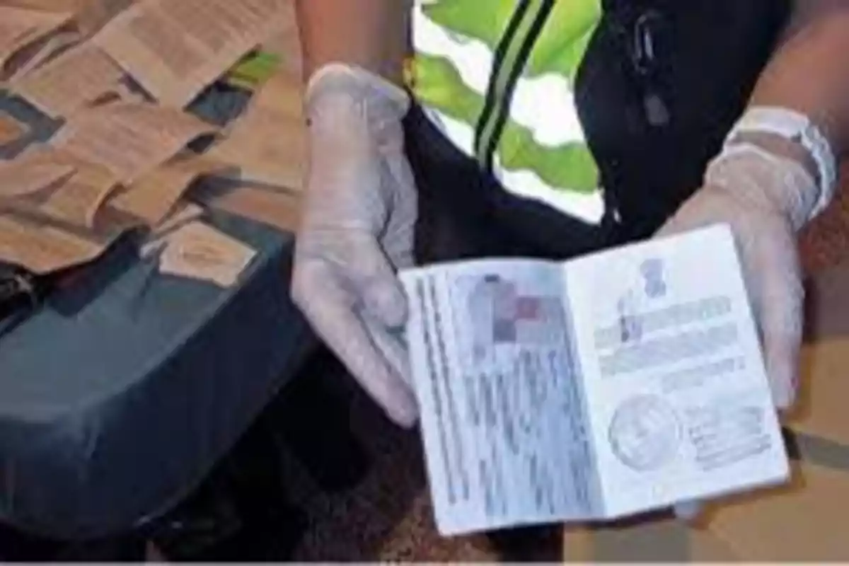 Persona con guantes sosteniendo un pasaporte abierto sobre una mesa con documentos.