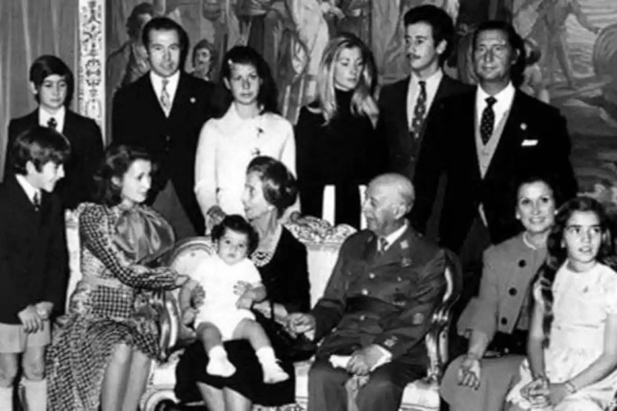Una familia numerosa posa para una fotografía en blanco y negro, con varias generaciones presentes, incluyendo adultos, jóvenes y un bebé, todos vestidos de manera formal.