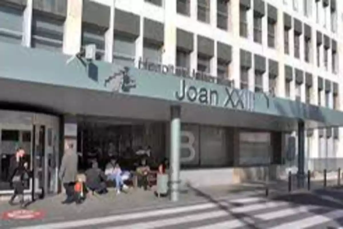Fachada del Hospital Universitari Joan XXIII con personas caminando y sentadas en la entrada.