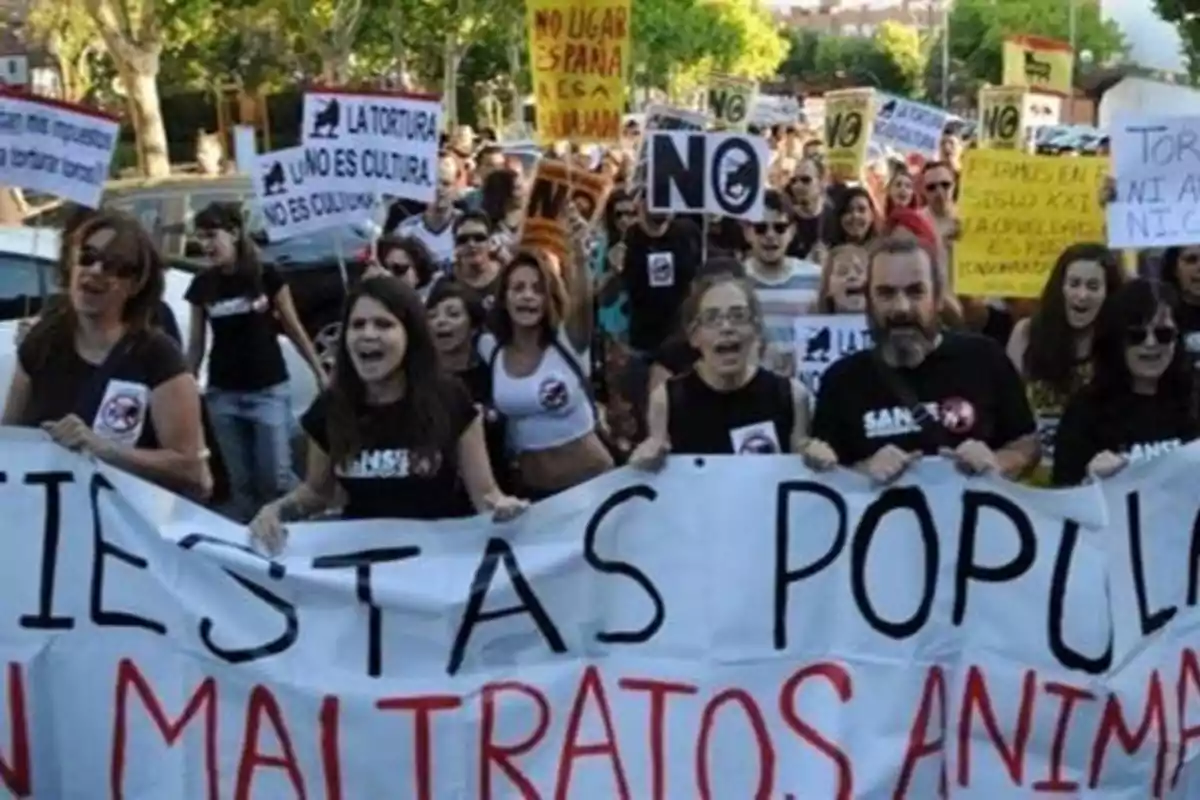 Un grupo de personas participa en una manifestación en contra del maltrato animal, sosteniendo pancartas y carteles con mensajes como "La tortura no es cultura" y "Fiestas populares sin maltratos animales".