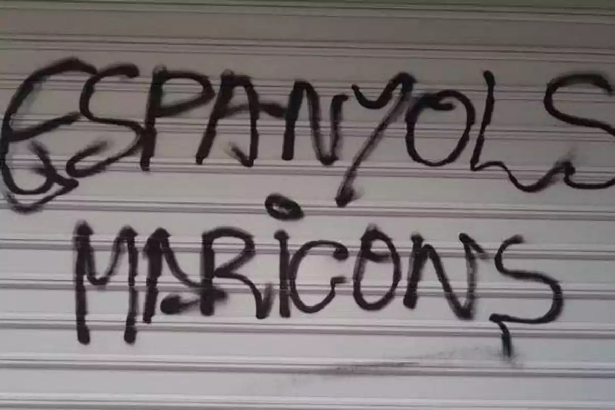 Grafiti en una persiana metálica con un mensaje ofensivo.
