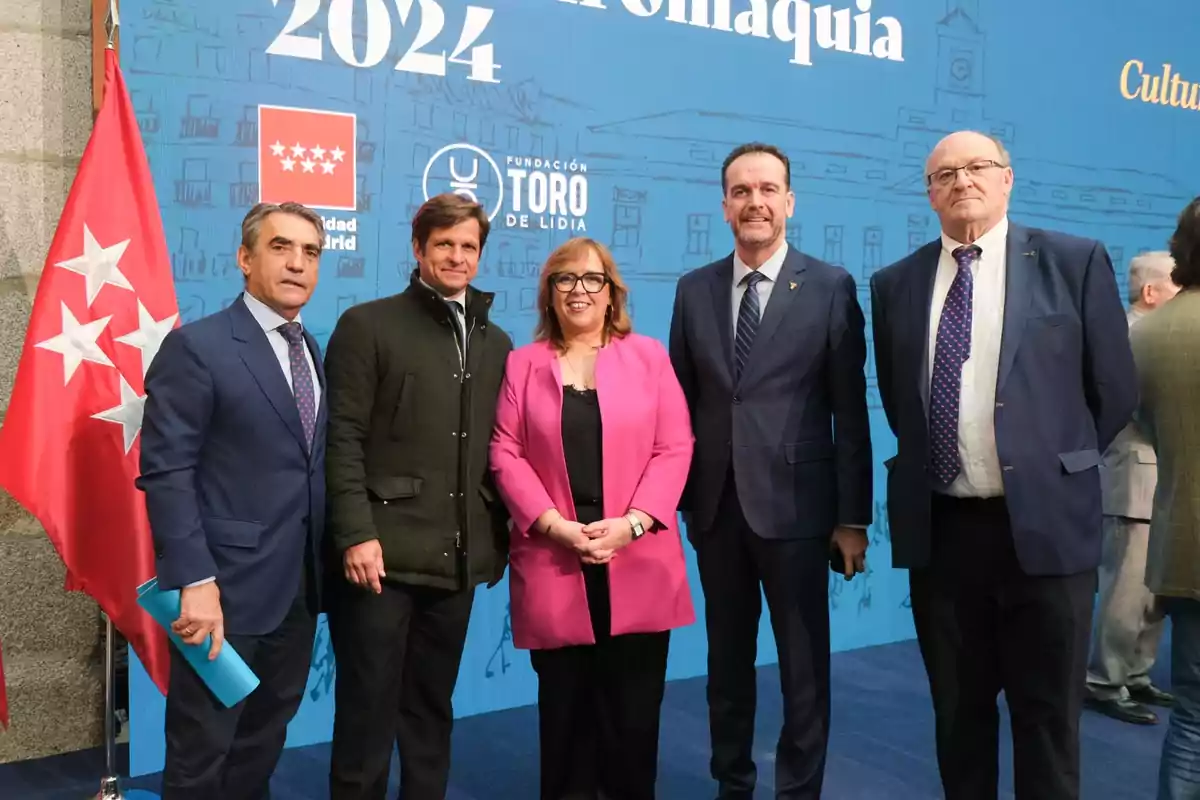 Un grupo de personas posando frente a un fondo azul con una bandera roja a la izquierda.