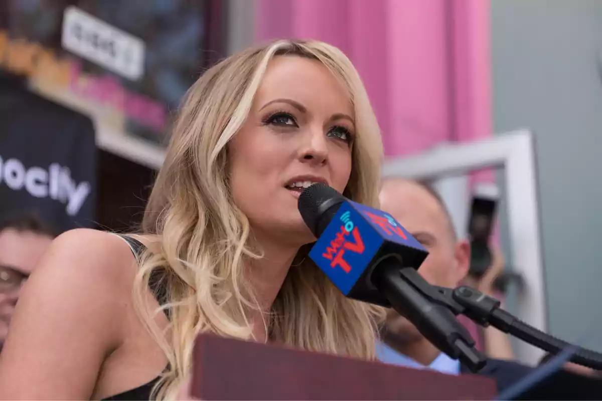 Una mujer rubia hablando en un micrófono durante un evento al aire libre.