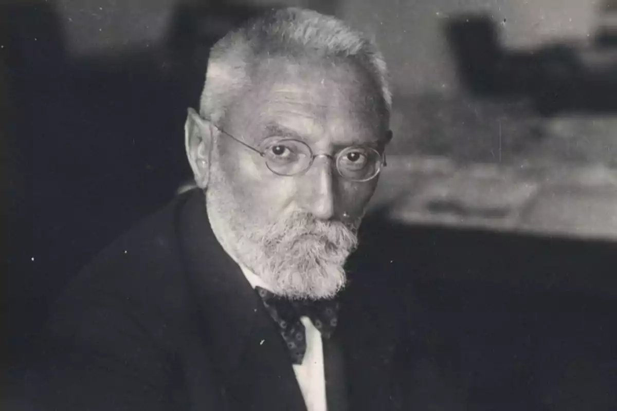 Hombre mayor con barba y gafas, vestido con traje y pajarita, en una fotografía en blanco y negro.