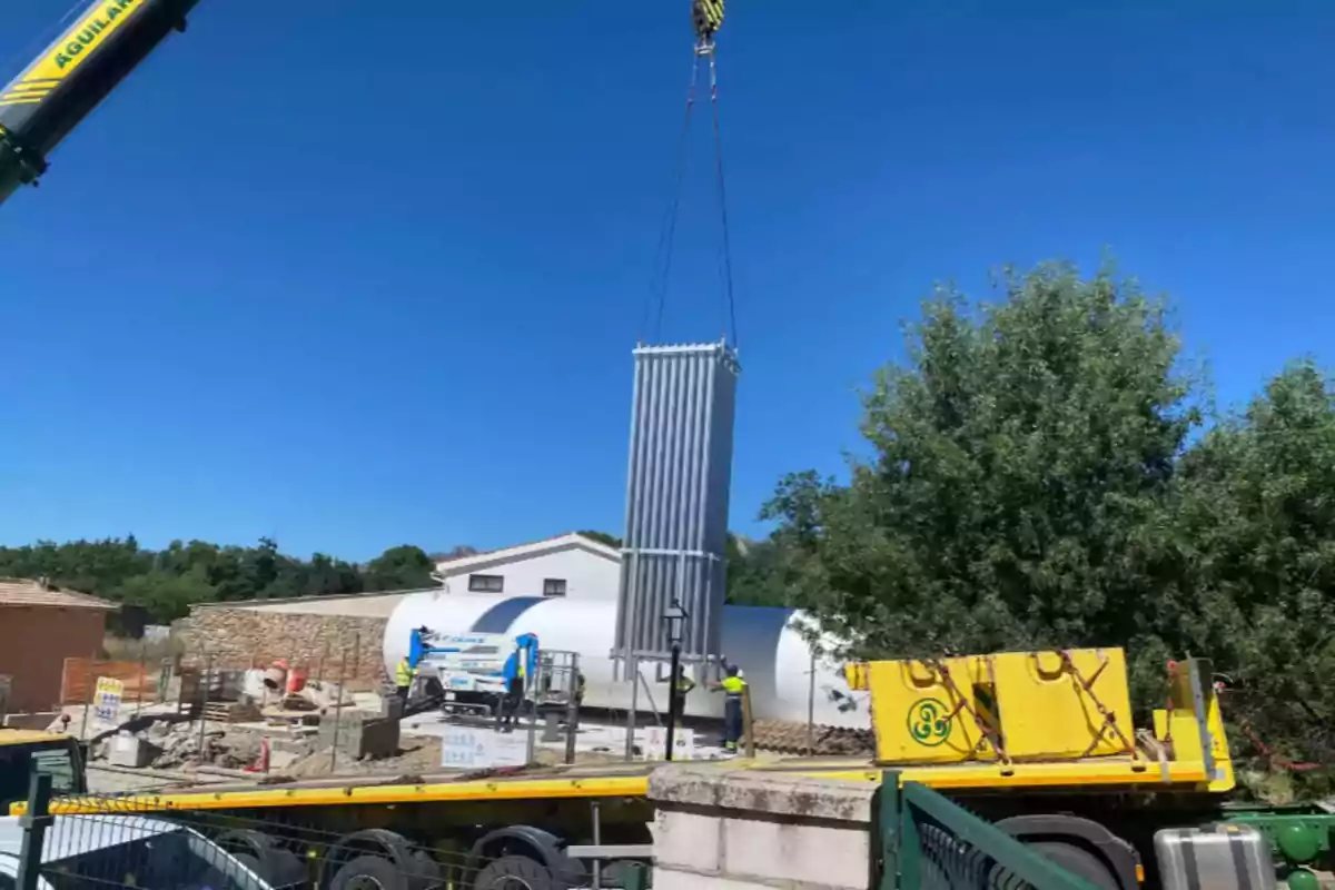 Grúa levantando un gran equipo industrial en una zona de construcción al aire libre con trabajadores y maquinaria alrededor Grúa levantando un gran equipo industrial en una zona de construcción al aire libre con trabajadores y maquinaria alrededor
