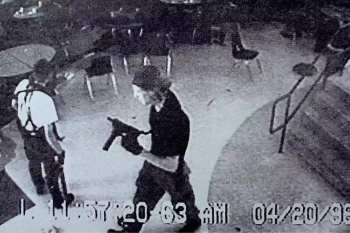 Dos personas armadas caminando en un área con mesas y sillas, captadas por una cámara de seguridad el 20 de abril de 1999.