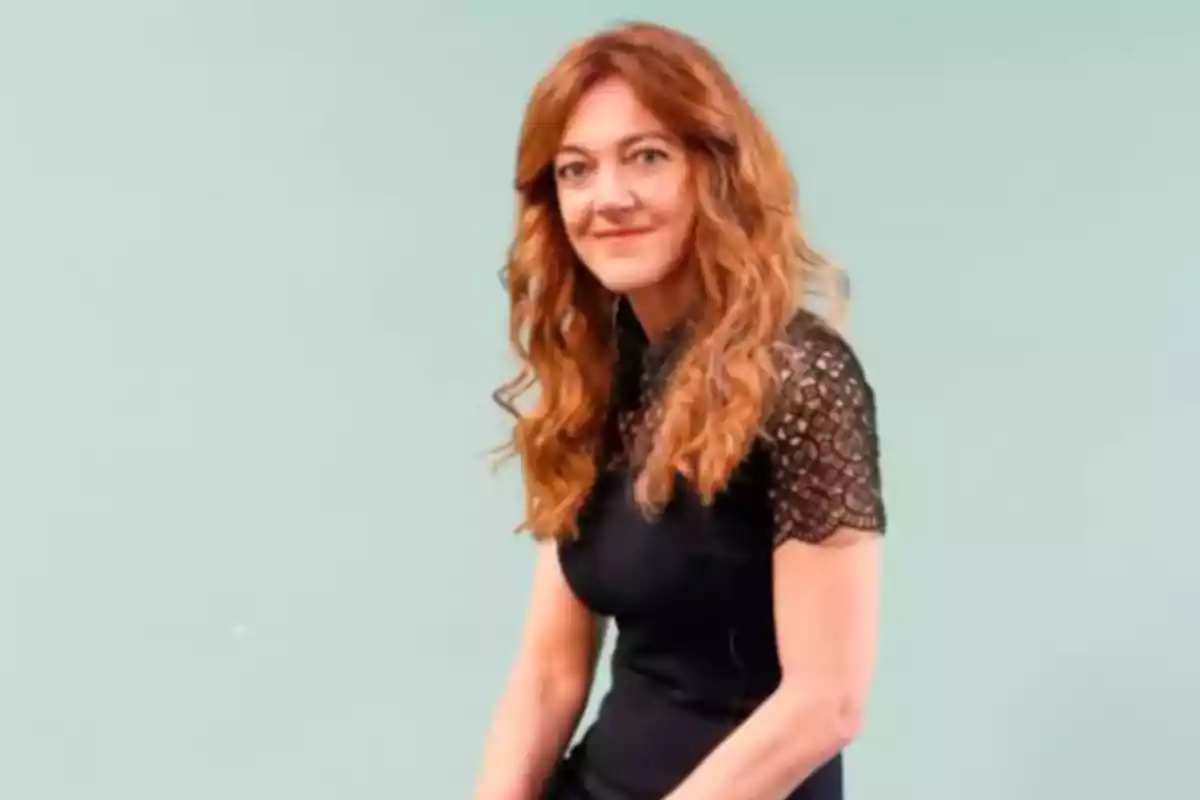 Mujer con cabello largo y rizado de color castaño claro lleva un vestido negro con mangas de encaje y está sentada frente a un fondo verde claro. Mujer con cabello largo y rizado de color castaño claro lleva un vestido negro con mangas de encaje y está sentada frente a un fondo verde claro.