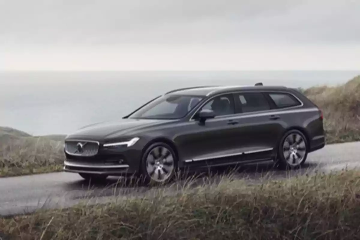 Un Volvo V90 T6 familiar negro circulando por un camino costero con el mar de fondo.