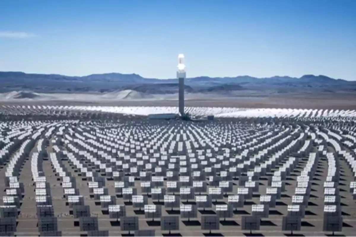 Planta de energía solar con numerosos paneles solares y una torre central en un paisaje desértico.