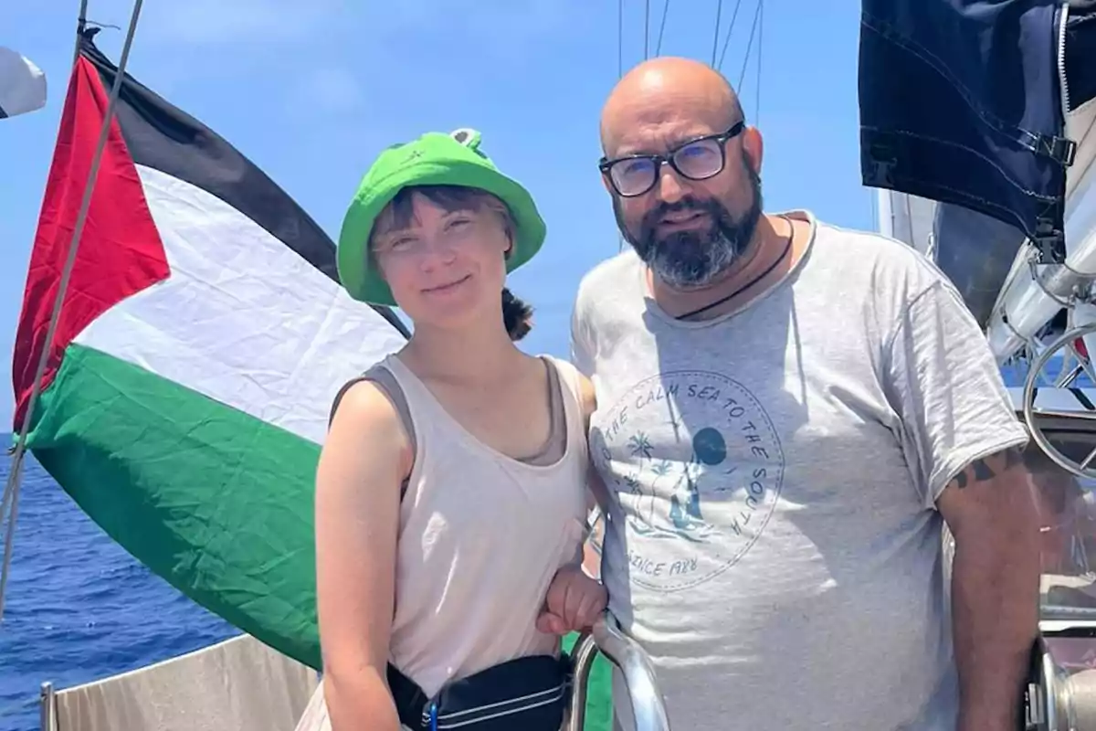 Dos personas posan en un barco con una bandera de Palestina al fondo en un día soleado