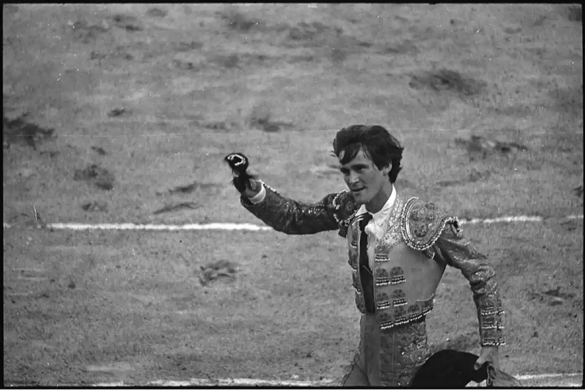 Un torero joven vestido con traje de luces sostiene un trofeo en la mano mientras camina por la arena de una plaza de toros Un torero joven vestido con traje de luces sostiene un trofeo en la mano mientras camina por la arena de una plaza de toros