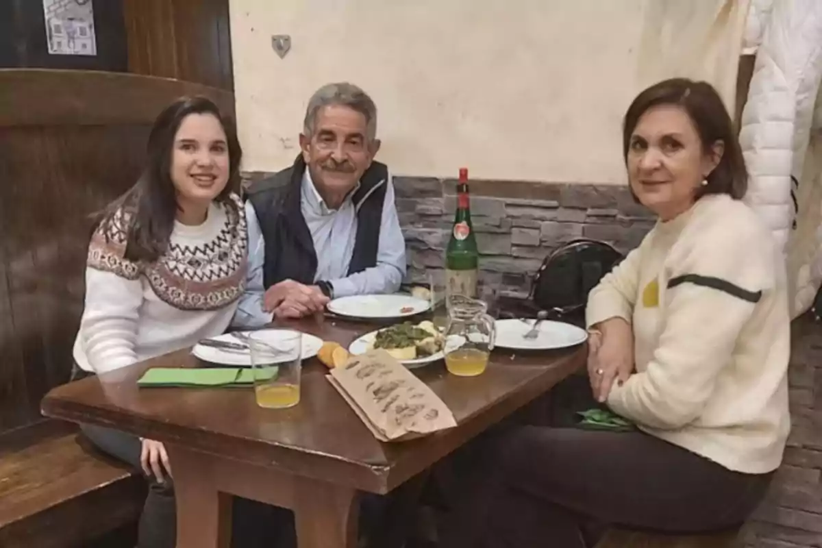 Tres personas sentadas alrededor de una mesa en un restaurante, con platos y bebidas frente a ellos, posan para la foto mientras sonríen. Tres personas sentadas alrededor de una mesa en un restaurante, con platos y bebidas frente a ellos, posan para la foto mientras sonríen.