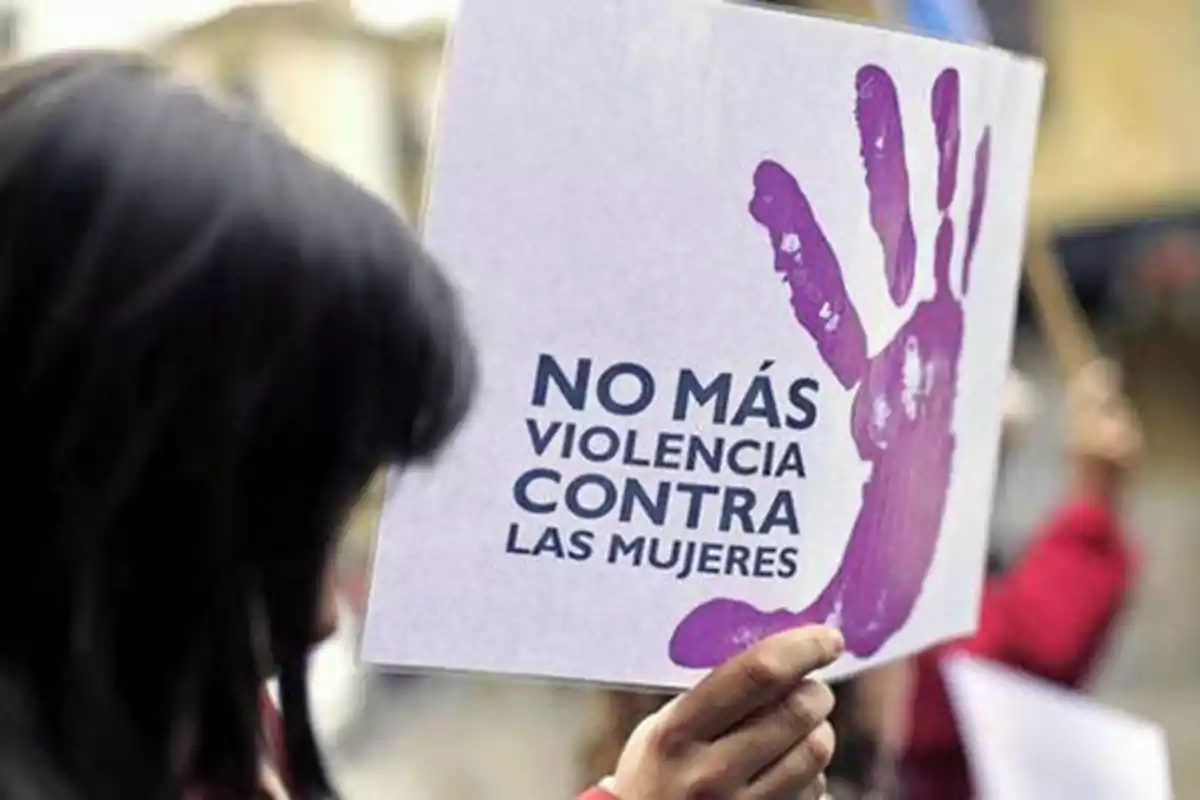 Persona sosteniendo un cartel con una mano morada impresa y el mensaje "No más violencia contra las mujeres".