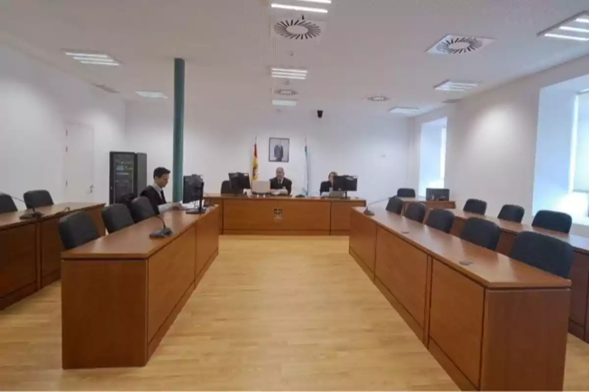 Una sala de tribunal con escritorios de madera y sillas negras donde se encuentran varias personas trabajando frente a computadoras.