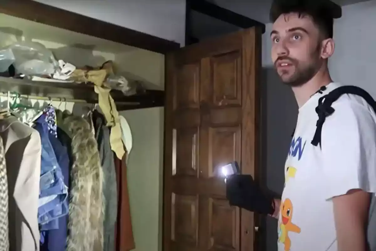 Persona con linterna explorando un armario lleno de ropa en una habitación oscura.