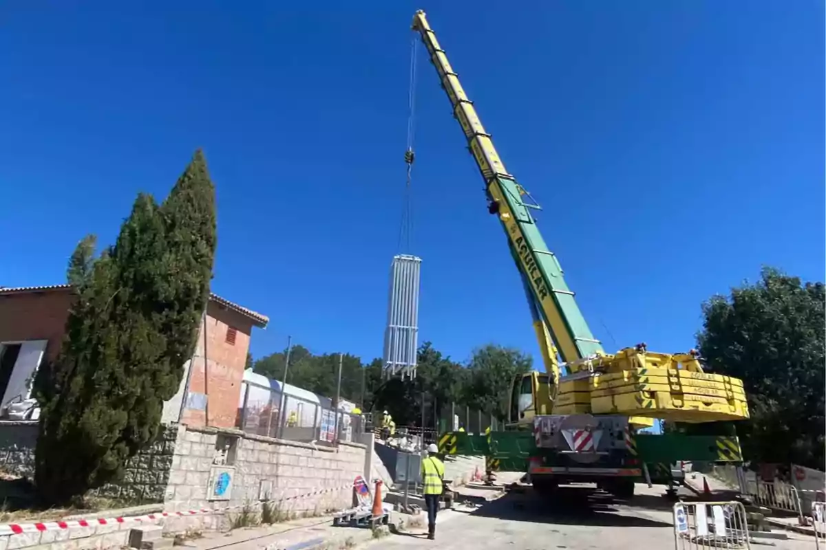 Grúa amarilla levantando una estructura metálica en una zona de construcción al aire libre con cielo despejado Grúa amarilla levantando una estructura metálica en una zona de construcción al aire libre con cielo despejado