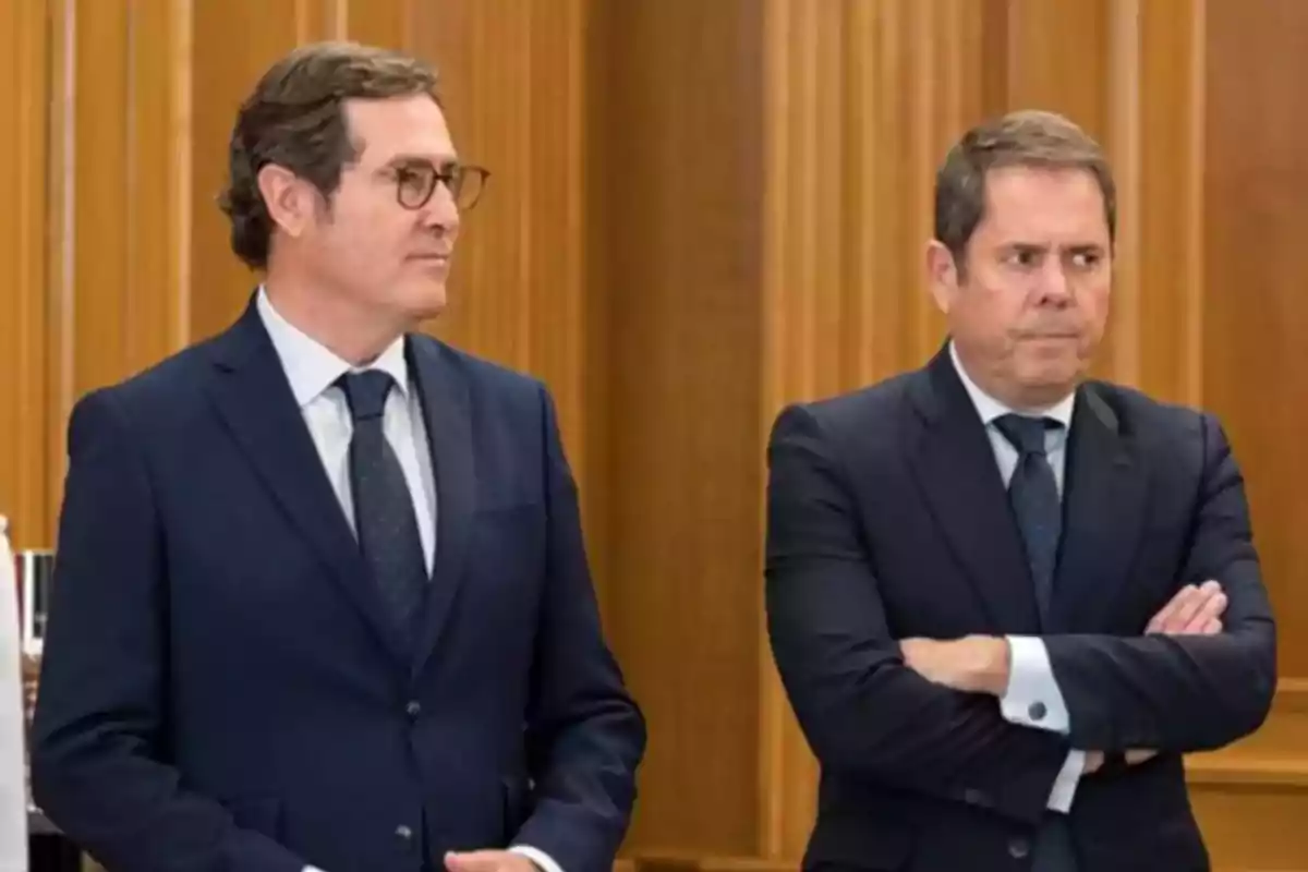 Dos hombres de traje oscuro en una sala con paneles de madera. Dos hombres de traje oscuro en una sala con paneles de madera.