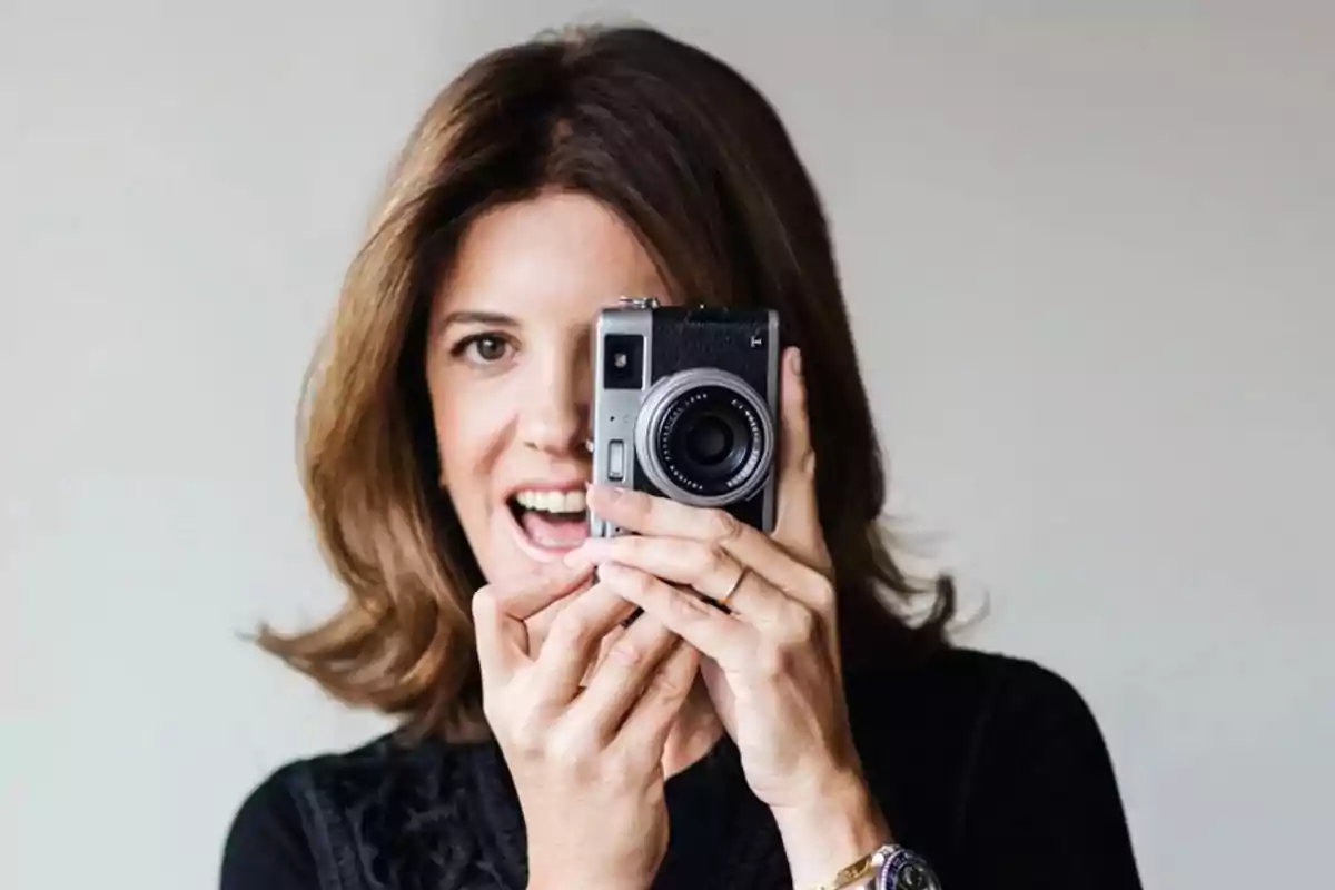 Mujer sonriendo mientras sostiene una cámara frente a su rostro.
