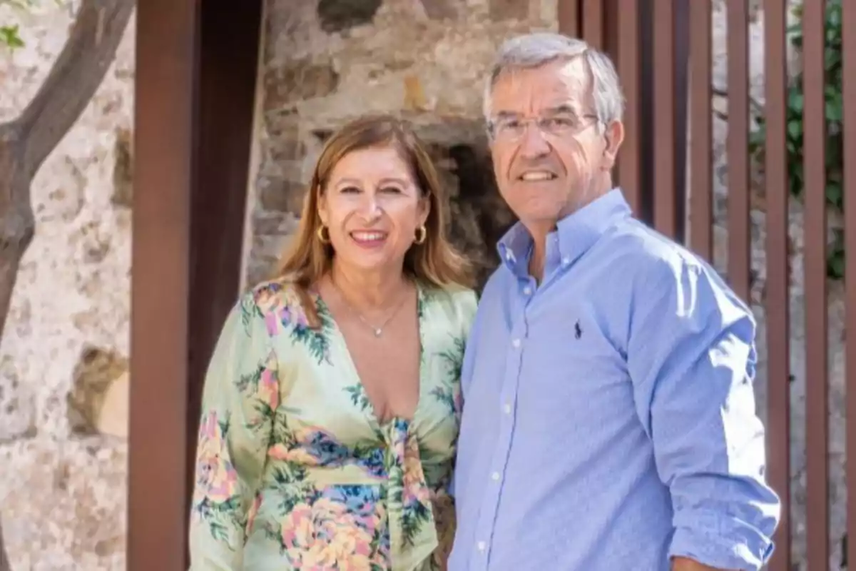 Una pareja sonriente posando al aire libre frente a una pared de piedra.