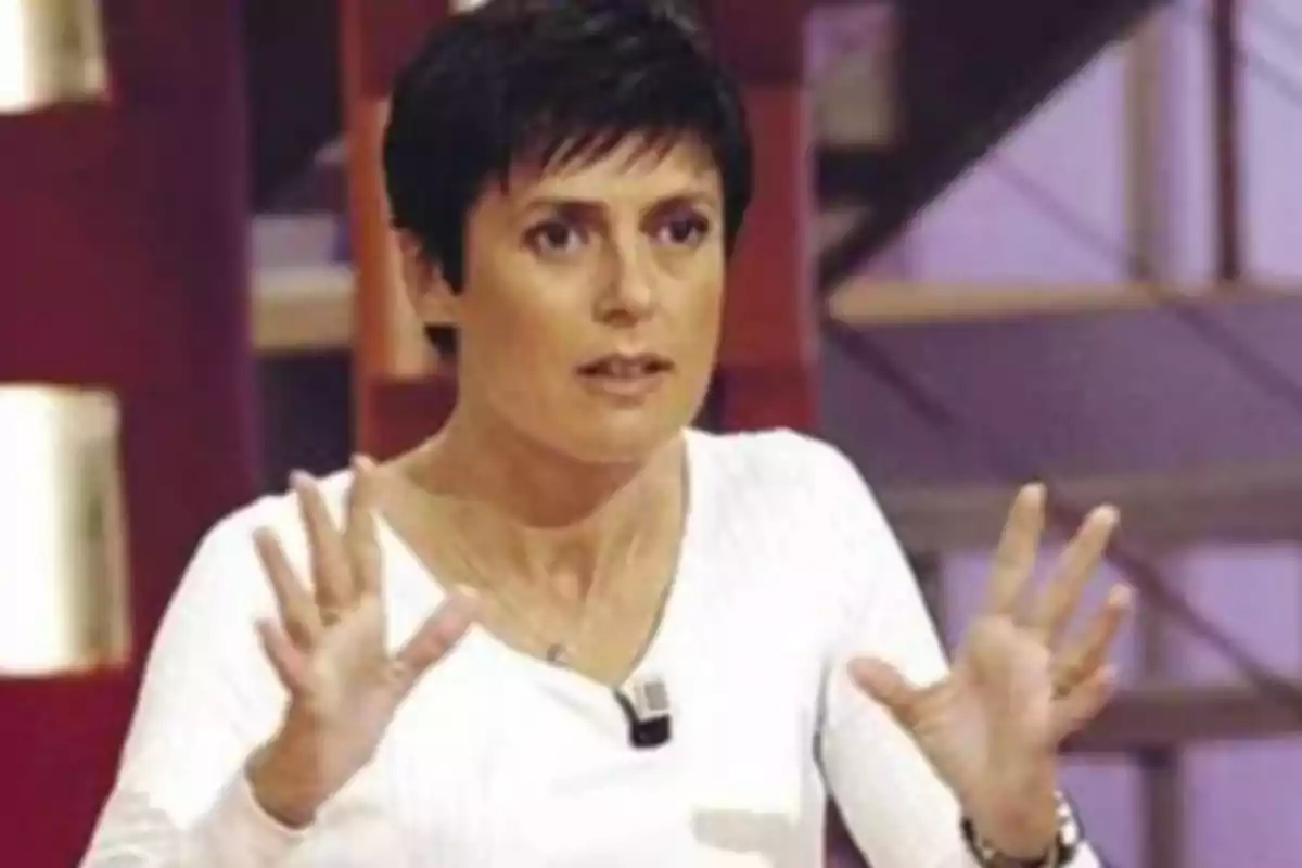Mujer de cabello corto y oscuro con camiseta blanca gesticulando con las manos en un estudio de televisión Mujer de cabello corto y oscuro con camiseta blanca gesticulando con las manos en un estudio de televisión