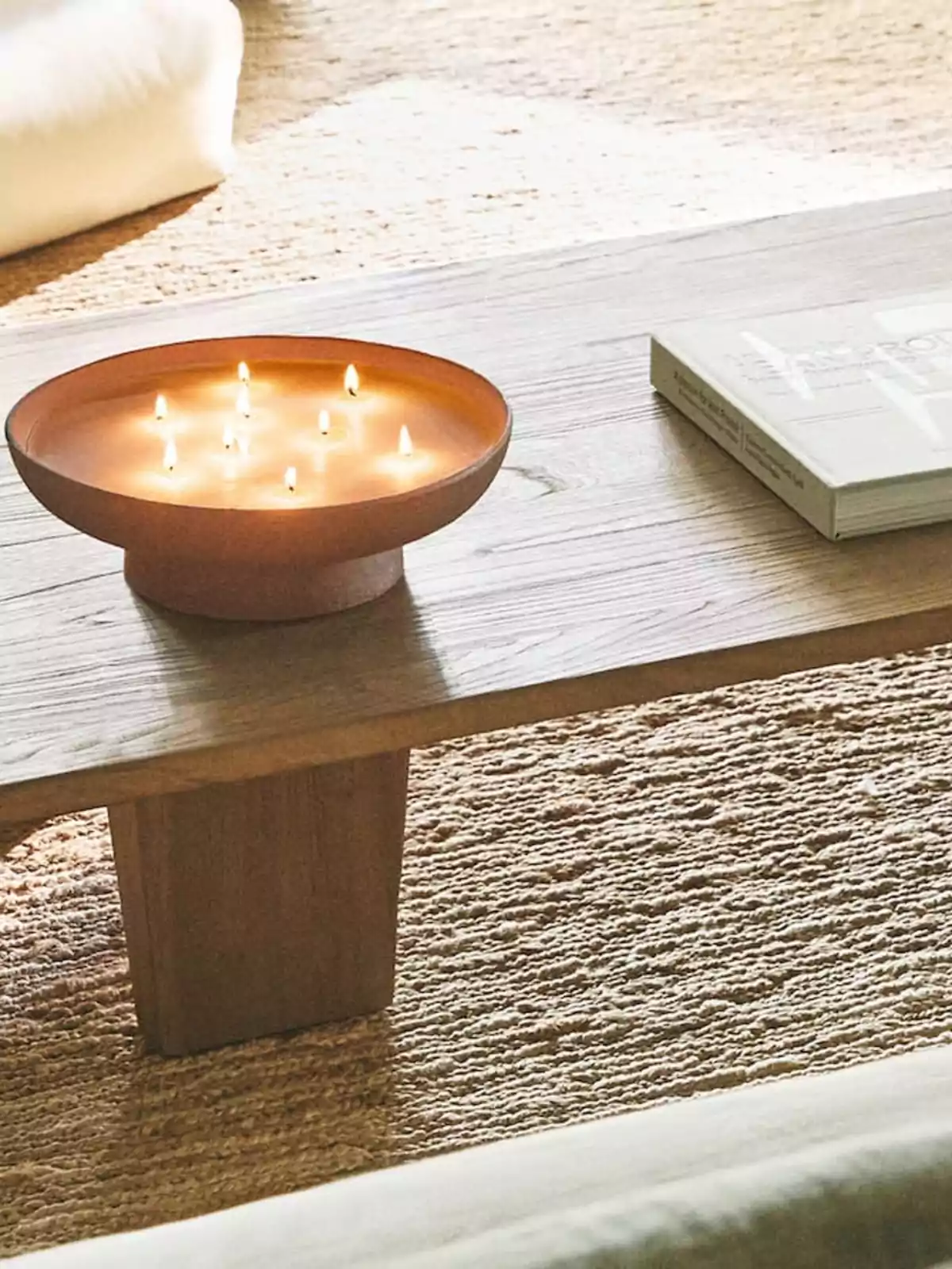 Una vela encendida con múltiples mechas y un libro sobre una mesa de madera.