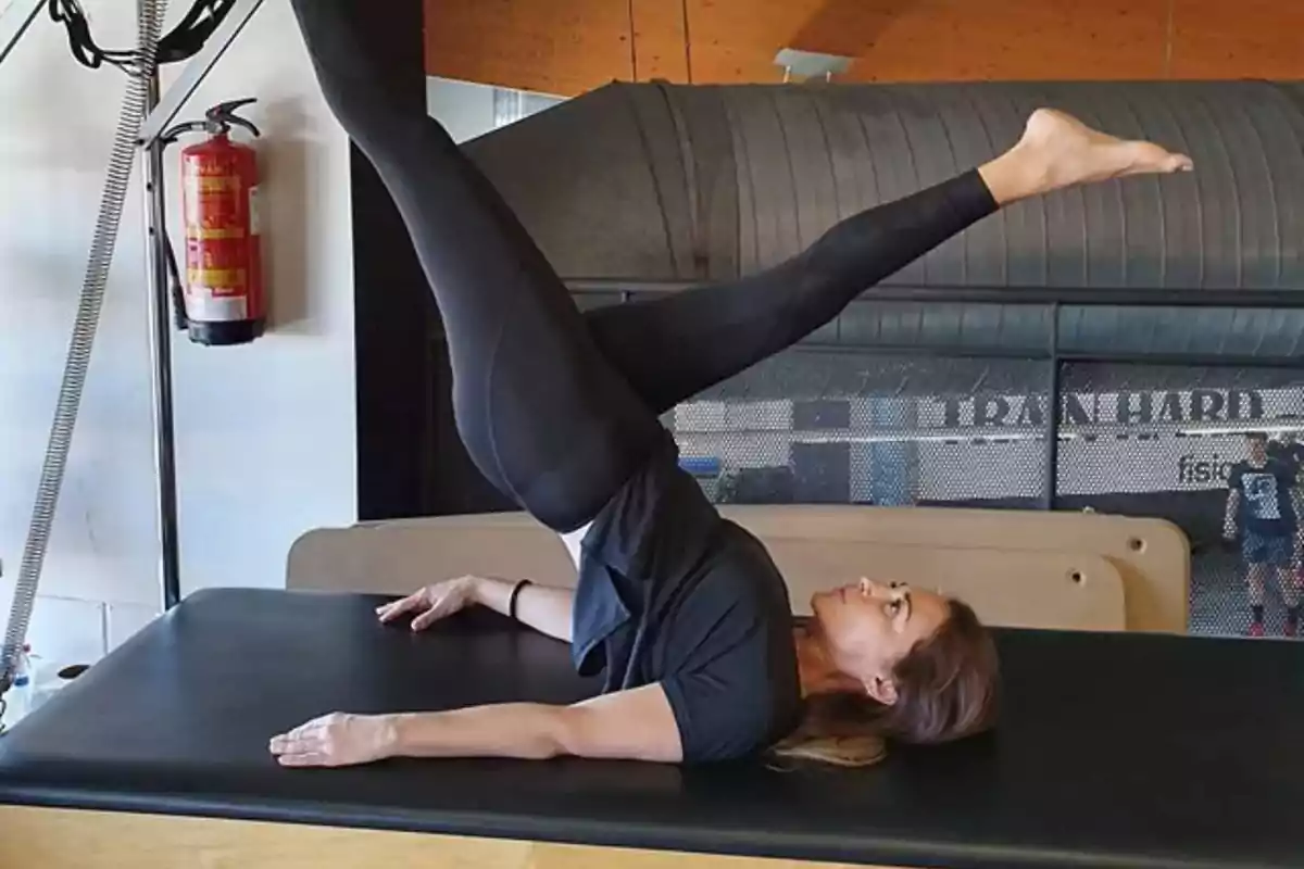Mujer realizando ejercicio de pilates en una camilla dentro de un gimnasio.