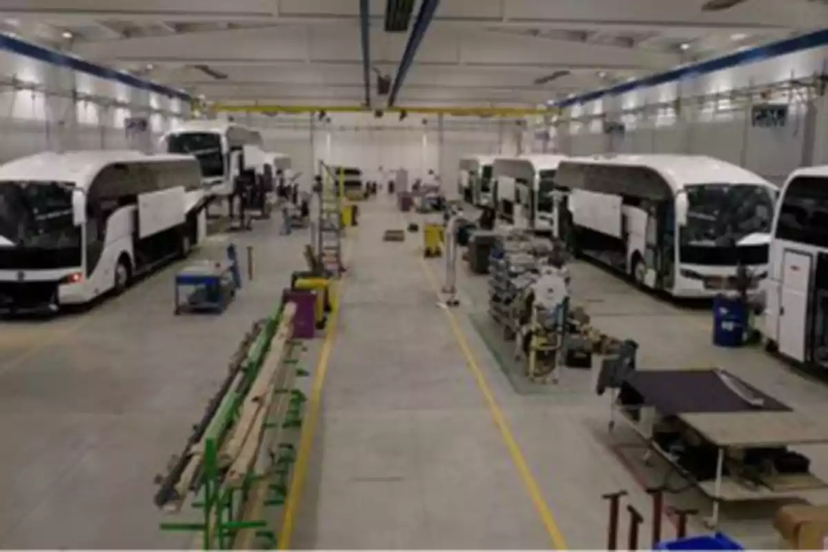 Fábrica de autobuses con varios vehículos en proceso de ensamblaje y herramientas distribuidas en el área de trabajo.